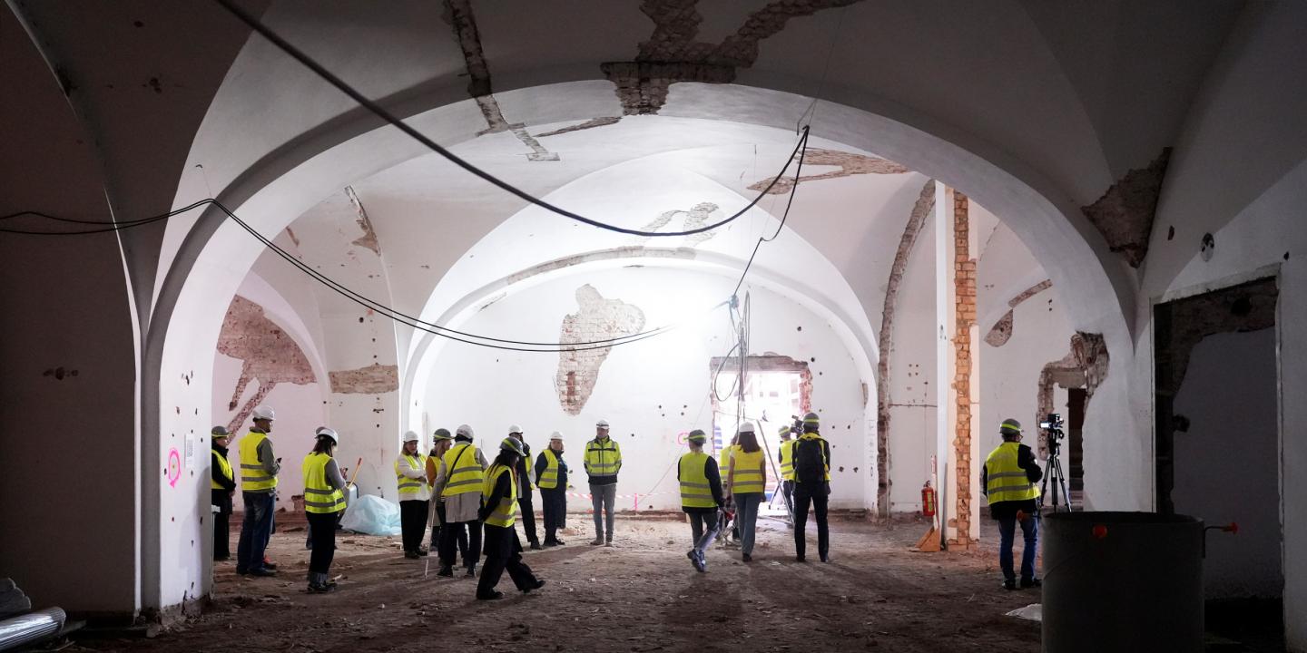 Group of people wearing helmets and vests explore a large historic hall during construction.