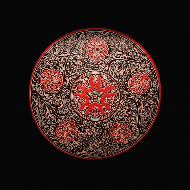 Red ceramic plate with black-and-white ornament and central star motif on a black background.
