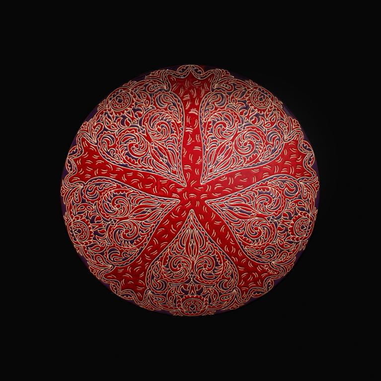 Sarkans dekoratīvs šķīvis ar sarežģītiem ornamentiem uz melna fona.