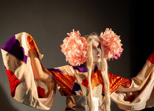 Performances mākslinieks krāšņā kostīmā ar teātra grimu uz skatuves.