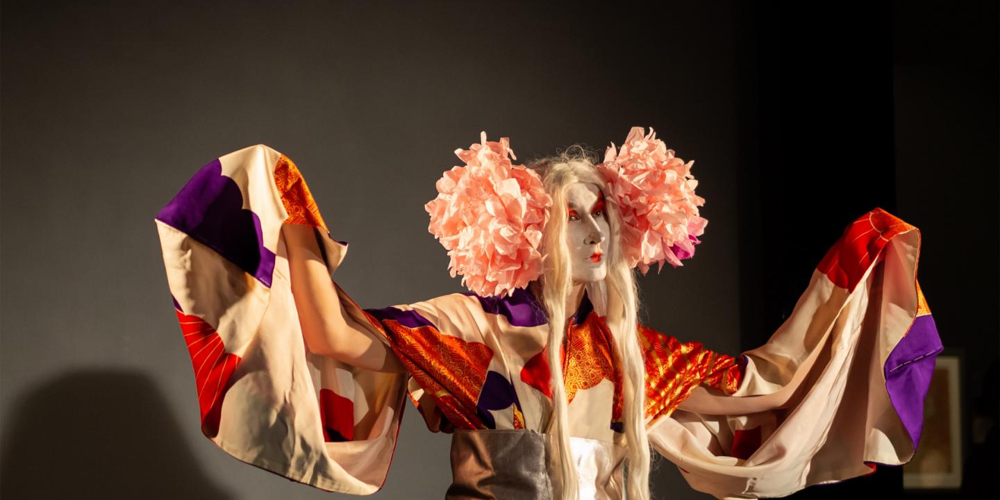 Performance artist in an elaborate costume with theatrical makeup on stage.
