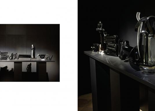 Tumšā ekspozīcijas telpā uz gara postamenta izgaismoti izvietoti melna un caurspīdīga stikla skulpturāli objekti, kas veido vienotu, ritmisku kompozīciju ar izteiktu gaismas un ēnas spēli.