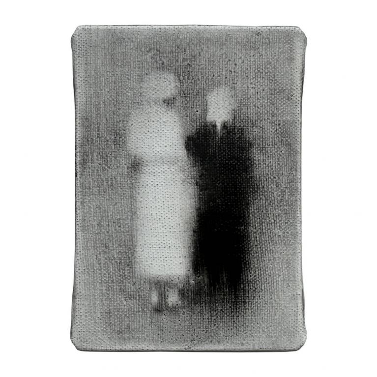 Nelielā, pelēcīgā attēlā izplūdušas divu cilvēku figūras stāv blakus, viena gaišāka, otra tumšāka, radot neskaidru, spokainu efektu.