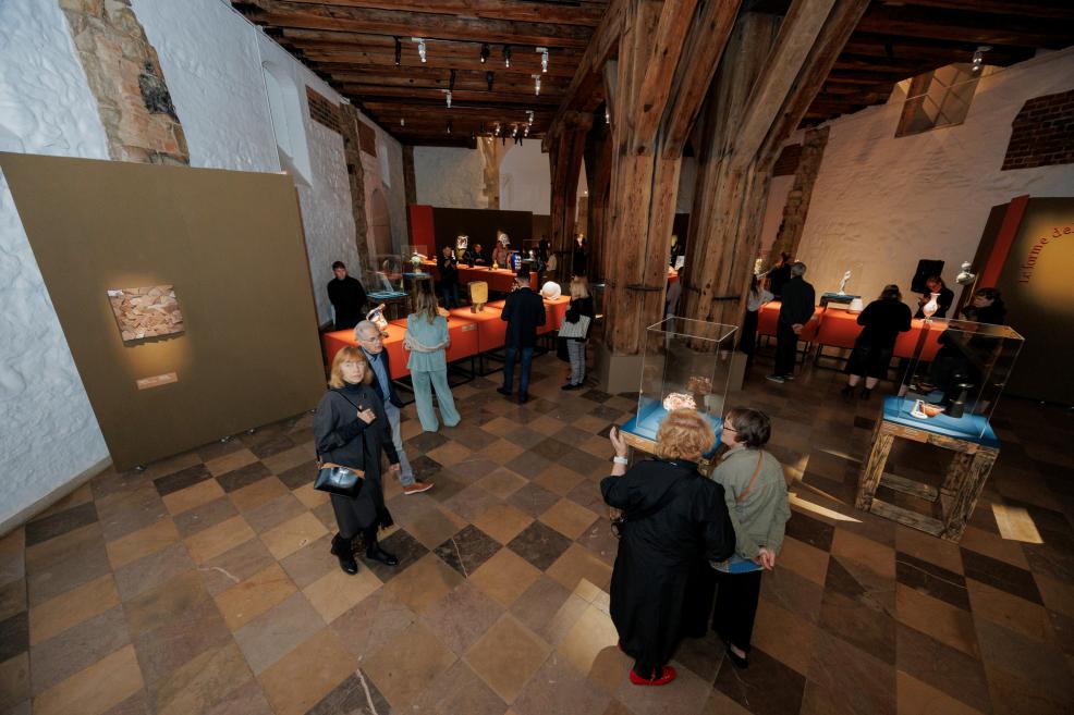 A spacious museum exhibition hall with wooden beams, red display cases, and several visitors viewing the exhibition.