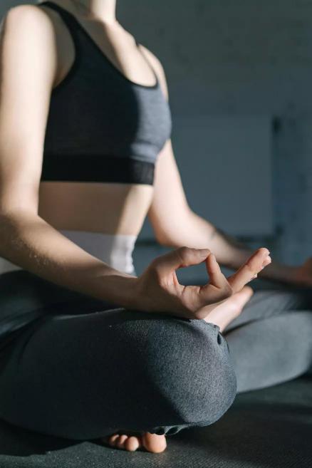 A person sits cross-legged on a mat in a meditation pose, holding a hand in jnana mudra while sunlight illuminates the body and clothing.