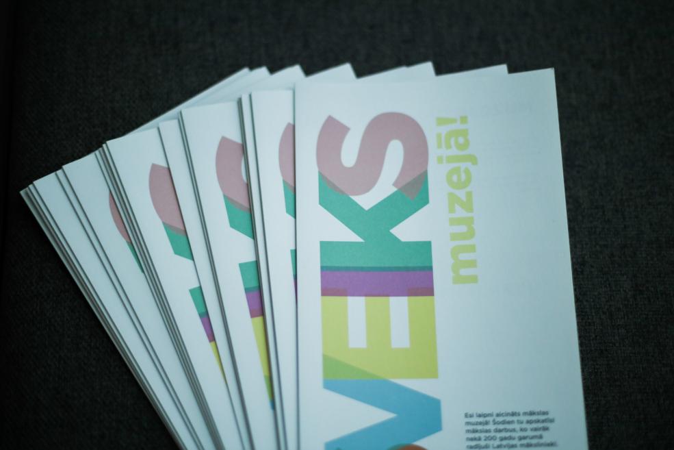 Kaudzītē sakārtotas krāsainas muzeja izglītojošās kartītes ar uzrakstu “Sveiks muzejā!”.