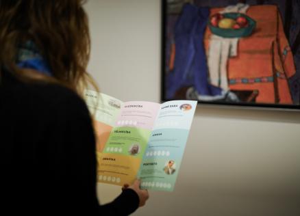 Cilvēks rokās tur vairākas krāsainas drukātas kartītes ar uzrakstu “Sveiks muzejā!”.