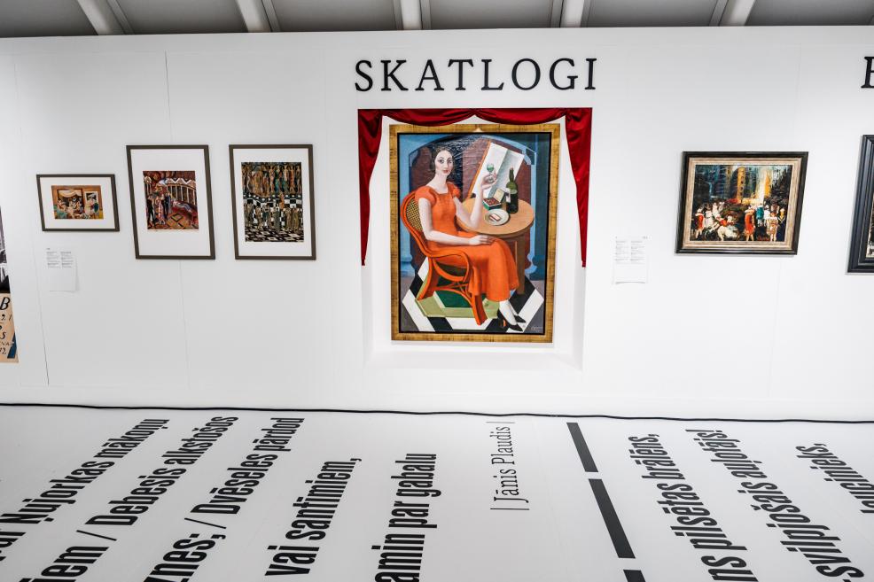 Exhibition view with the wall heading “Skatlogi”, a central painting of a seated woman framed by red drapery, and other artworks displayed on the wall.