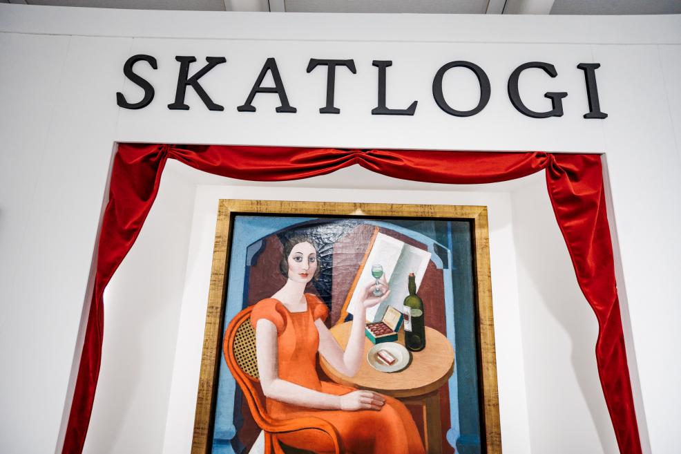 Exhibition section “Skatlogi” with the wall heading “Skatlogi” and a centrally displayed painting framed by decorative red drapery.