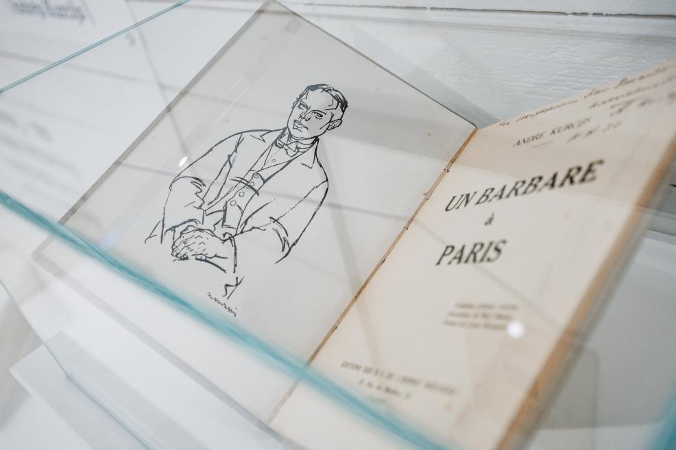 An open book displayed in a glass case, featuring a graphic illustration of a man and a French title page reading “Un barbare à Paris”.