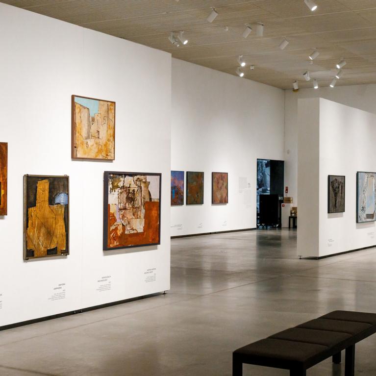 Muzeja izstāžu zāle ar vairākiem abstraktiem mākslas darbiem un soliņu apmeklētājiem.