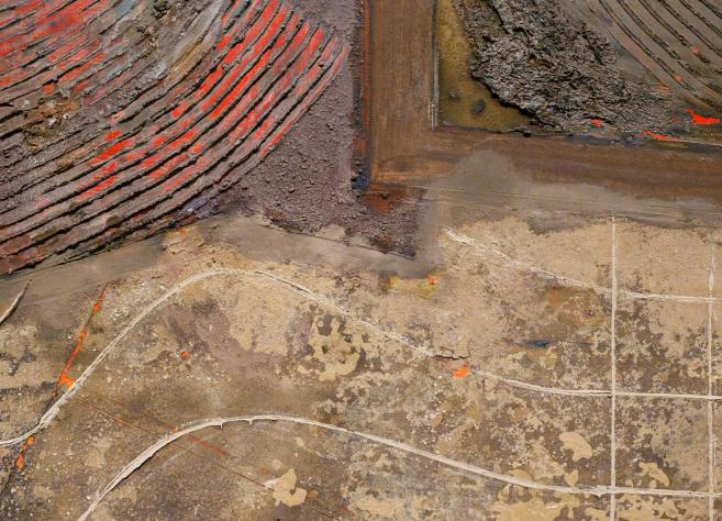 Abstrakta glezna ar teksturētu virsmu, zemes toņiem un sarkanām līnijām.