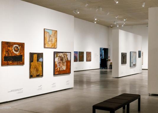 Muzeja izstāžu zāle ar vairākiem abstraktiem mākslas darbiem un soliņu apmeklētājiem.