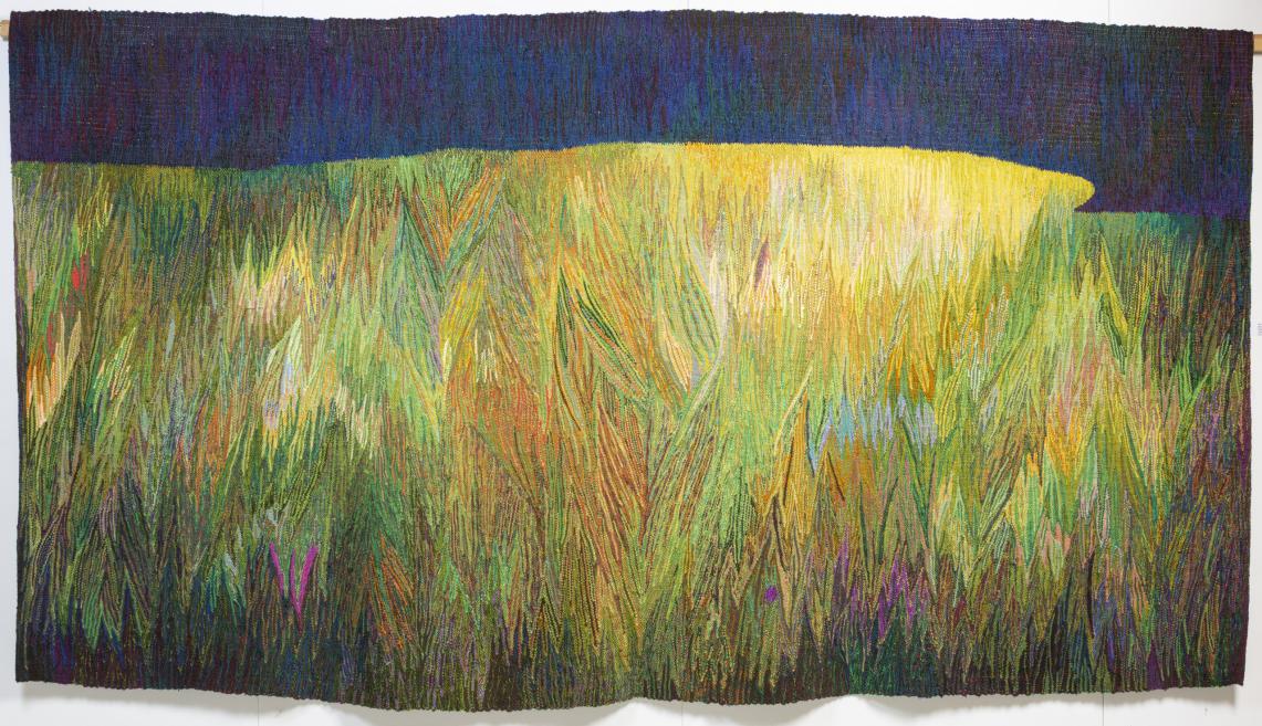 A large tapestry with an abstract landscape, where green and yellow field motifs transition into a dark blue sky band.A colorful tapestry depicting stylized blue and purple flowers on green stems against a pastel background.