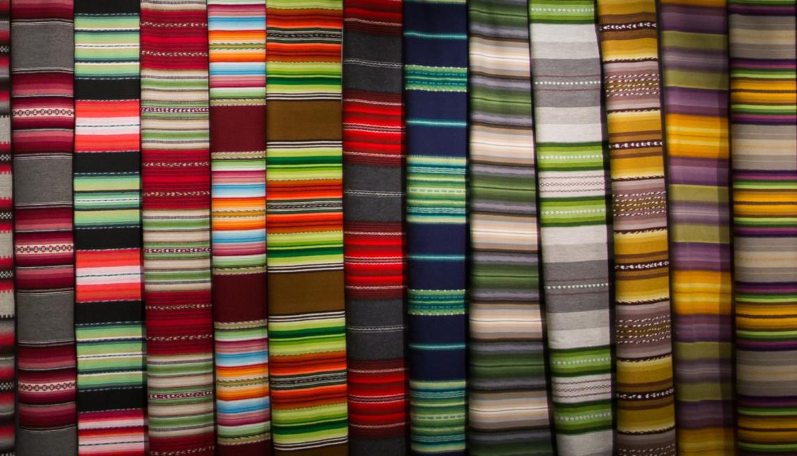 Brightly colored fabrics with horizontal stripes and traditional patterns are arranged in a row.