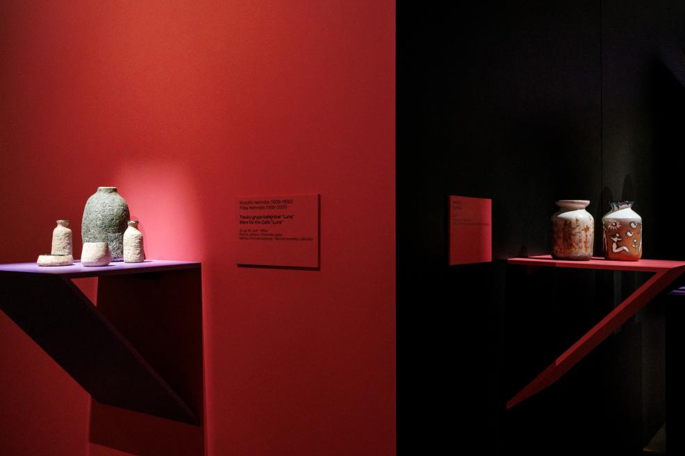 Several ceramic vases and vessels are displayed on red and black shelf structures in a museum exhibition.