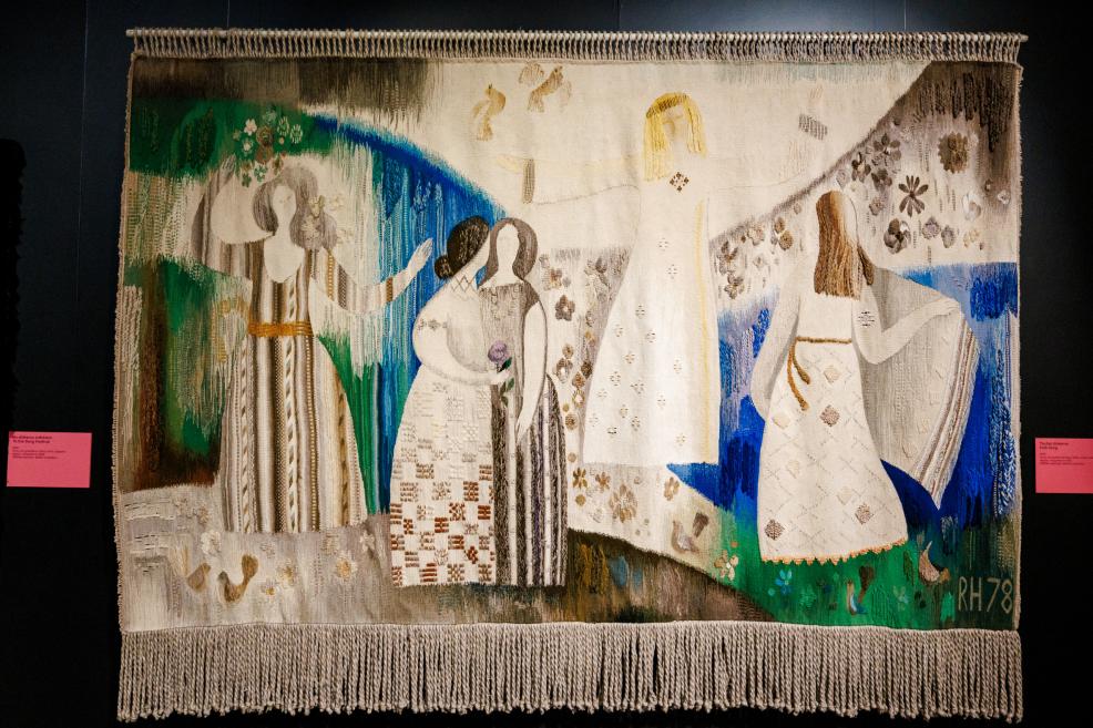 Woven textile artwork with four stylized female figures in white garments on a green, blue and beige background.