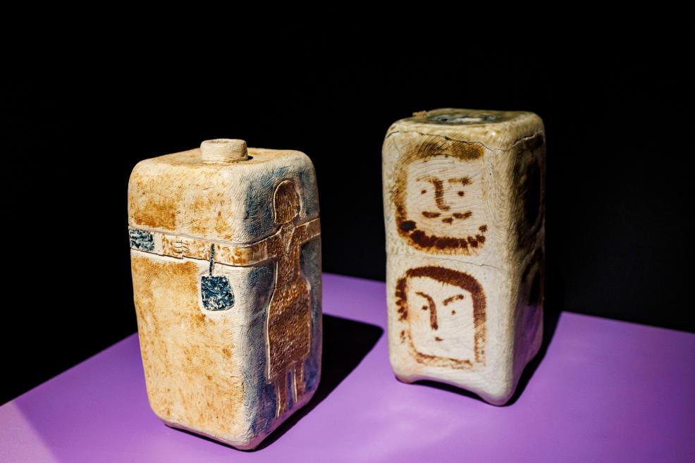 Two small rectangular ceramic or stone vessels with incised and painted ornament stand on a purple base against a black background.