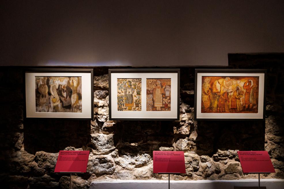 Three framed tapestry sketches displayed on a stone wall in a museum, each with a red label below.