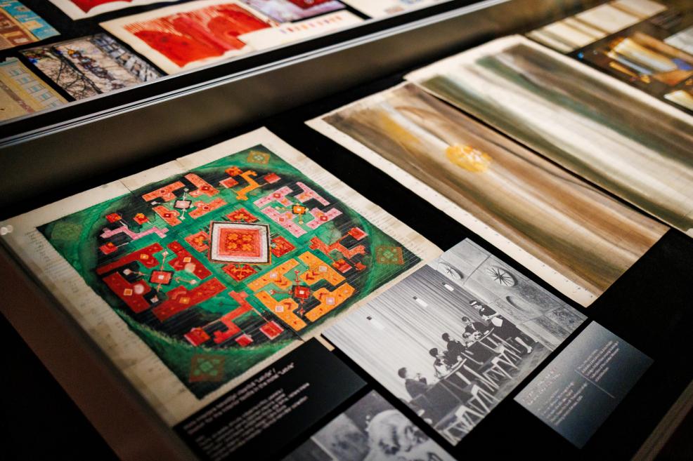Art reproductions and photographs displayed in a glass case, including a colorful geometric drawing and a black-and-white group seated at a table.