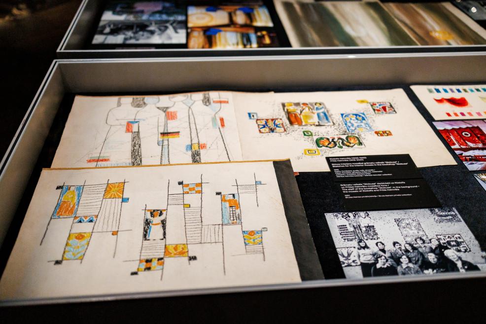 Drawings and prints with geometric color blocks, along with black-and-white photographs and information labels, are displayed in an exhibition case.