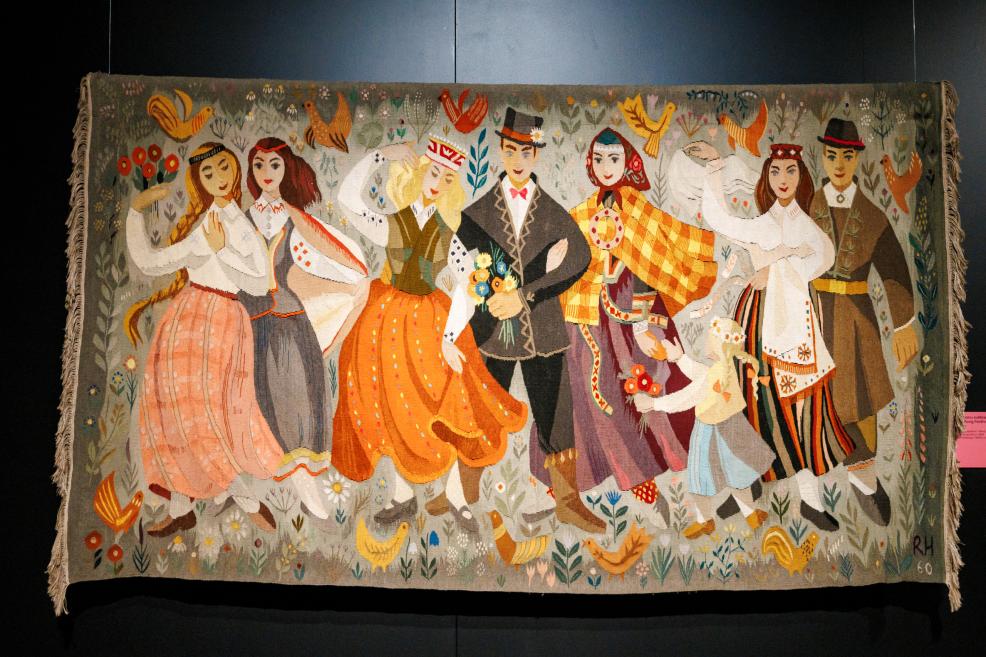 Colorful textile tapestry depicting a group of dancers and musicians in folk costumes, surrounded by birds and flowers.