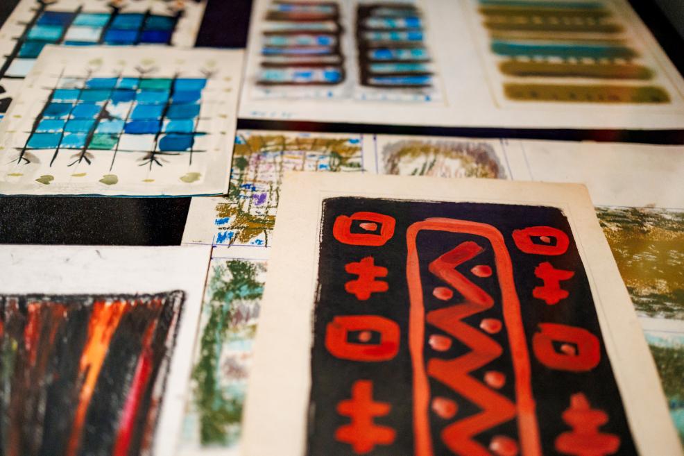 Several abstract colorful drawings and paintings on paper arranged in overlapping layers on a table.