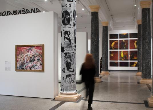Apmeklētāja pārvietojas pa plašu muzeja izstāžu zāli ar gleznām, grafikas darbiem un laikmetīgās mākslas ekspozīciju.