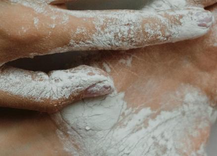 Tuvplānā redzamas ar baltu pulveri klātas rokas, kas veido un spiež mīkstu masu.