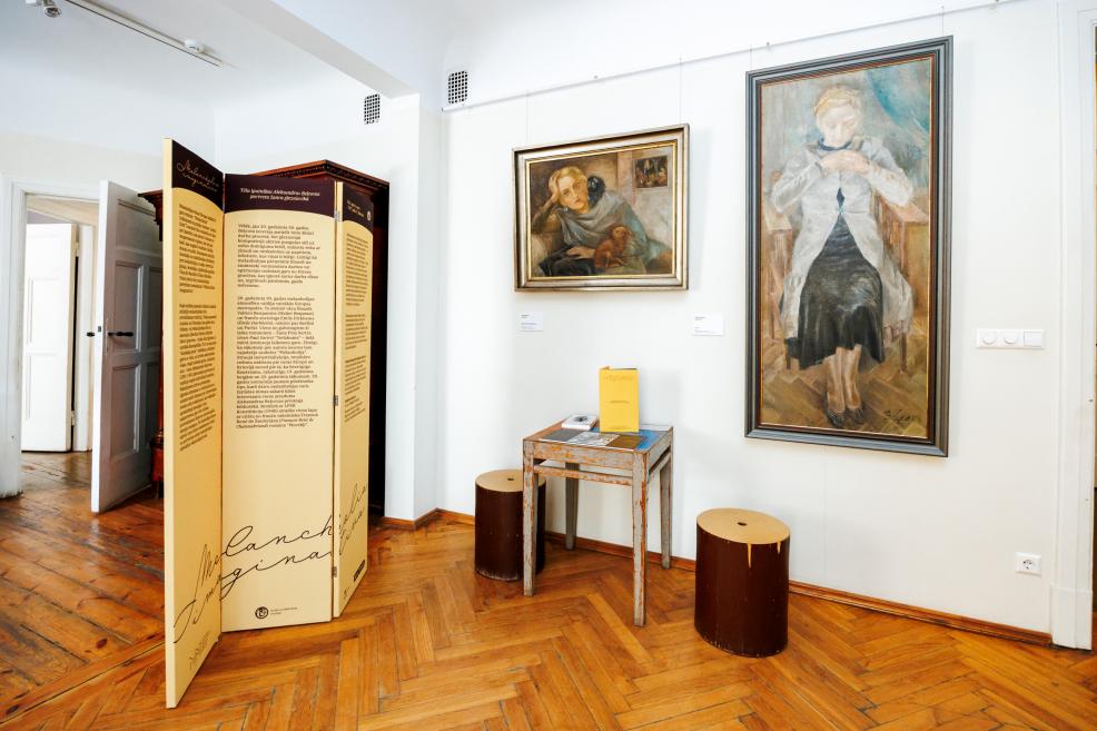 Muzeja telpā pie sienas izstādītas divas gleznas ar sieviešu portretiem, blakus informatīvs stends un neliels galds ar katalogu.