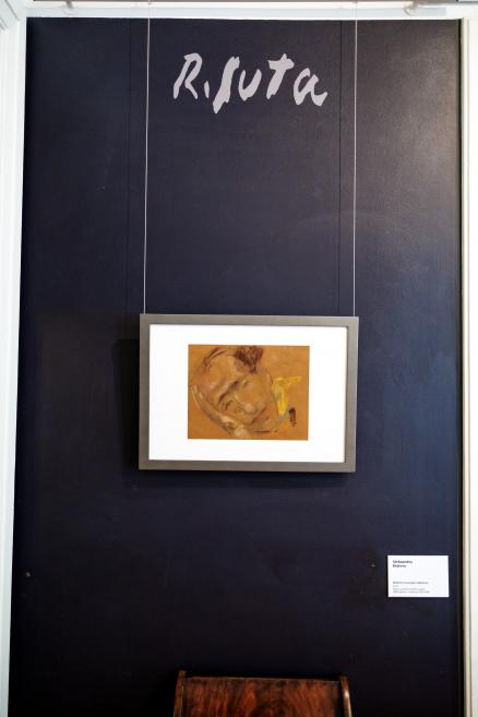 Tumši zilā sienā ar uzrakstu “Risuta” iekārts ierāmēts portreta zīmējums, blakus redzama neliela informācijas plāksne.