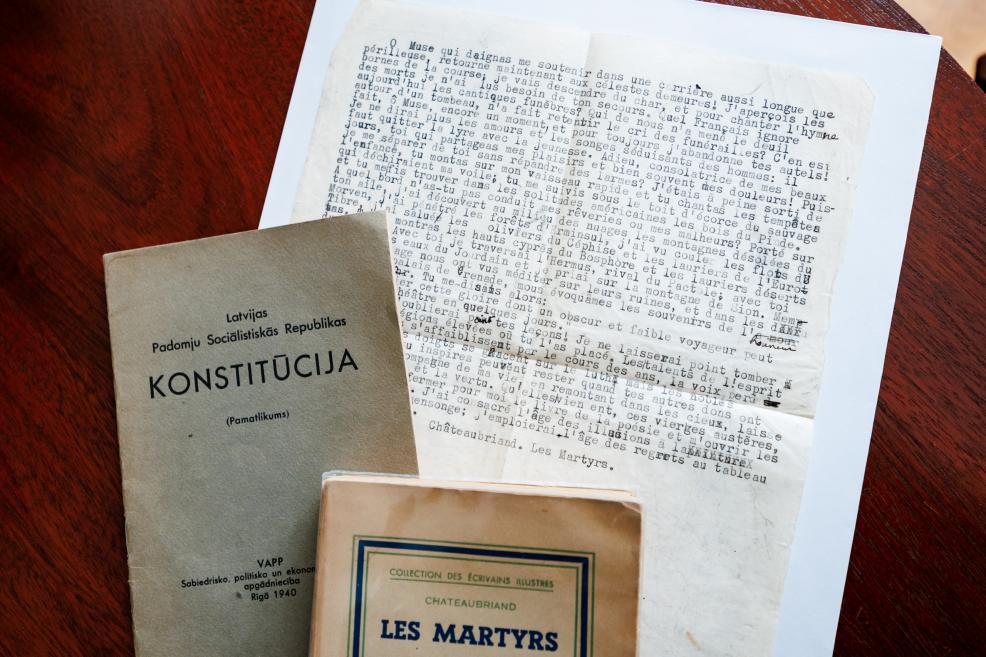 Uz galda novietoti dokumenti – Latvijas PSR konstitūcijas izdevums, franču teksts un grāmata “Les Martyrs”.