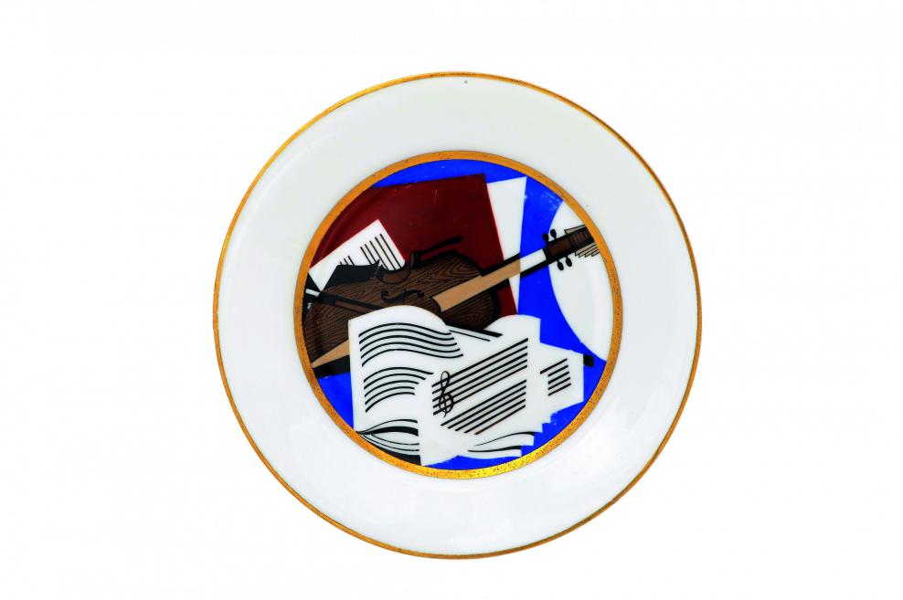 Dekoratīvs porcelāna šķīvis ar stilizētu mūzikas motīvu – notīm un stīgu instrumentu grafiskā kompozīcijā.
