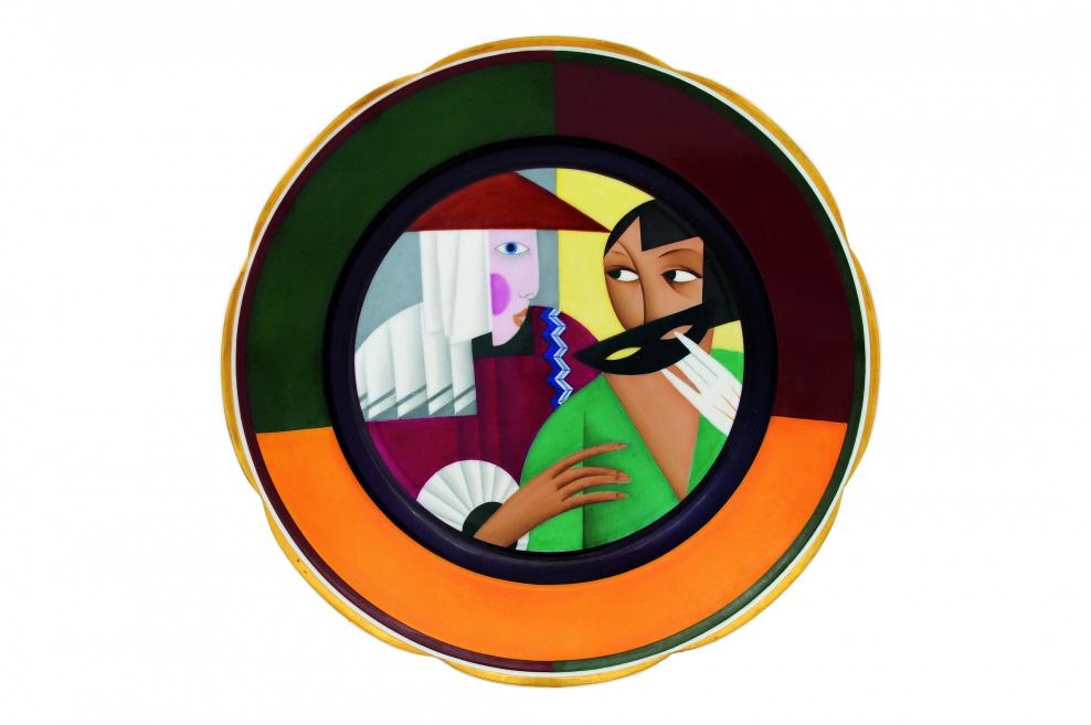 Dekoratīvs porcelāna šķīvis ar stilizētu figūru kompozīciju, kur attēlota sievietes figūra ar masku un ģeometriskiem krāsu laukumiem.