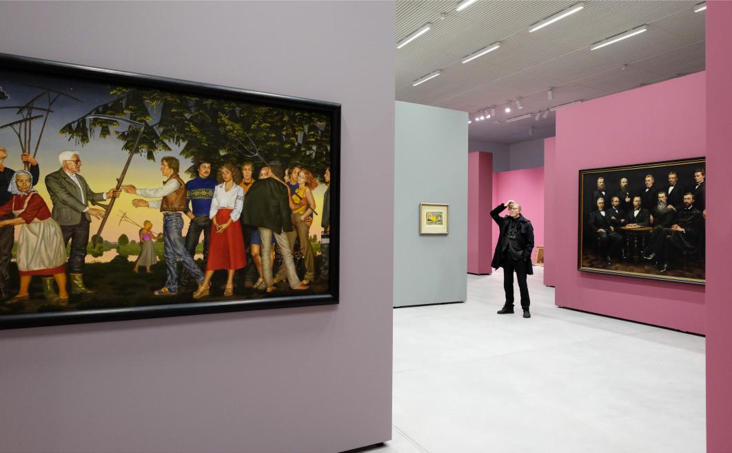 Muzeja izstāžu zāle ar gleznām uz sienām un apmeklētāju, kas stāv telpas vidū.