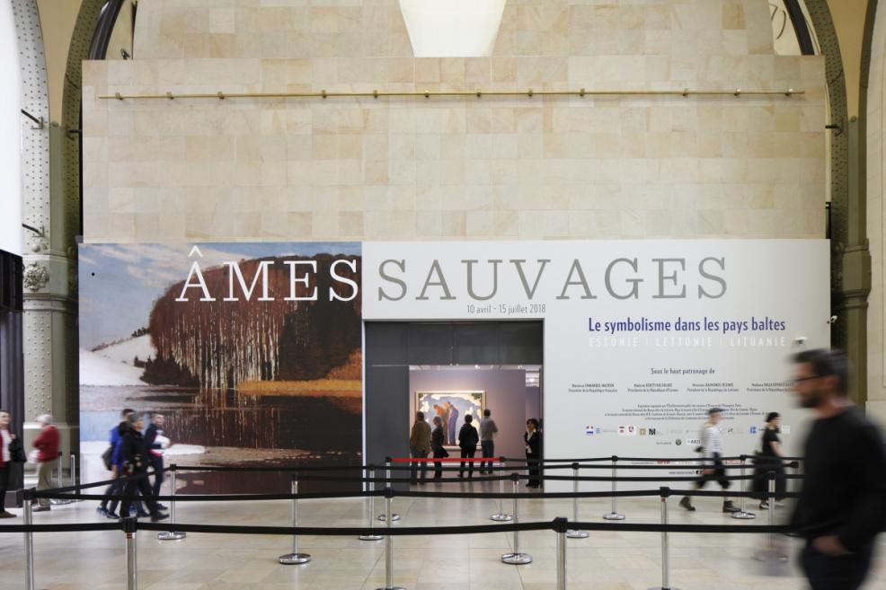 Izstādes “Âmes sauvages” ieeja ar lielu sienas grafiku un apmeklētājiem kustībā.