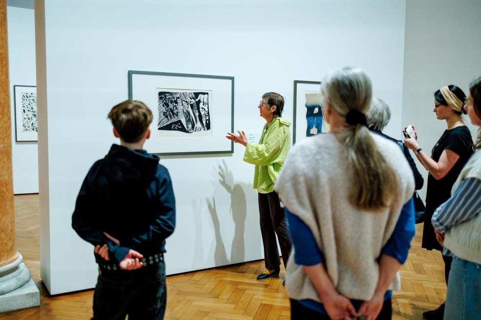 Gids muzejā skaidro grafikas darbu nelielai apmeklētāju grupai izstāžu zālē.