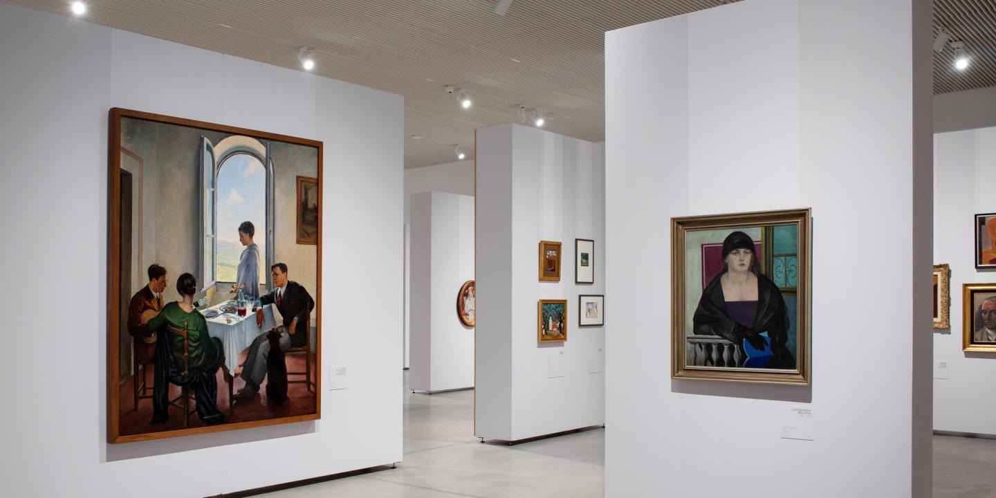 Muzeja izstāžu zāle ar gleznām pie baltām sienām, centrā redzamas figurālas kompozīcijas un portreti.