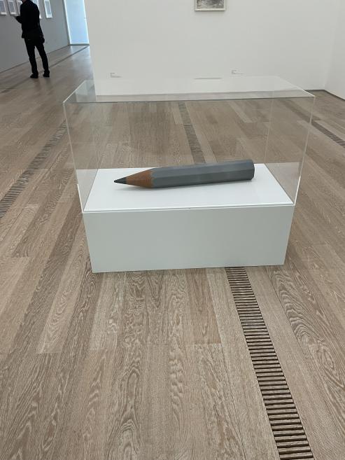 A sculptural pencil-shaped object displayed in a glass case in a contemporary art exhibition.