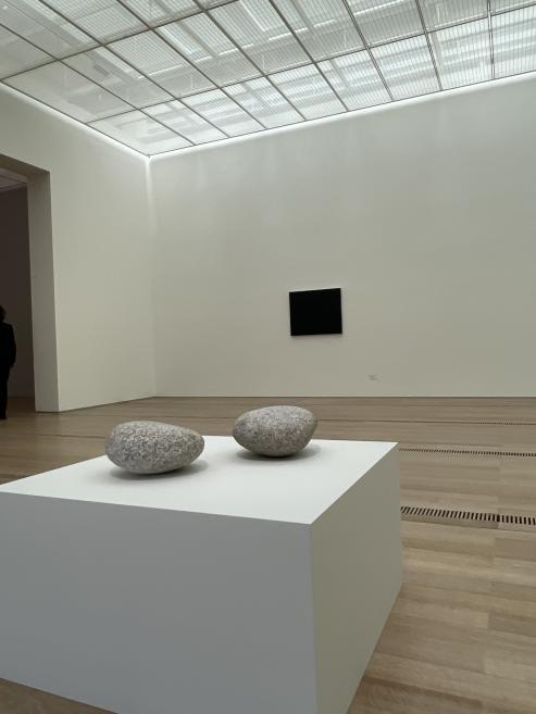 Two rounded stone objects displayed on a white plinth in a minimalist contemporary art gallery space.