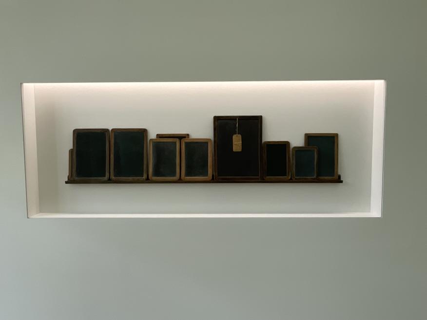 A composition of small framed objects and surfaces arranged in a wall niche with even lighting, creating an archival and contemplative installation.
