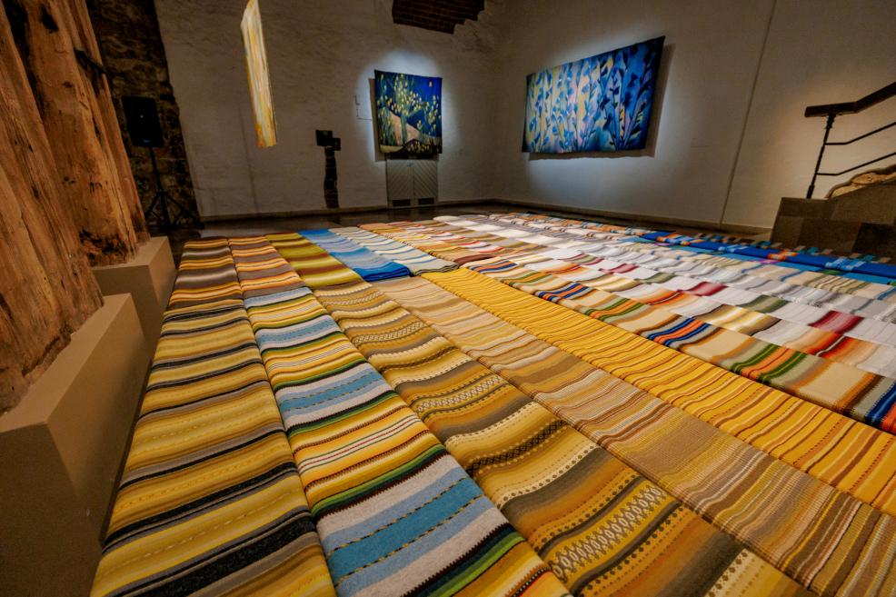 An exhibition space with multi-colored striped fabrics on the floor and blue floral motif tapestries on the walls.