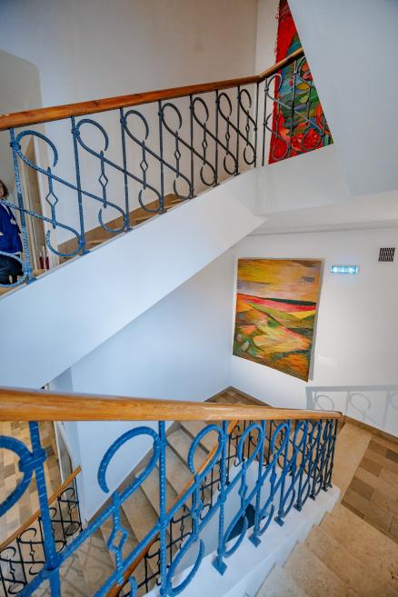 A museum staircase with blue metal railings and colorful tapestries displayed on the walls.