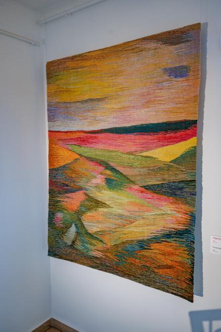 A colorful tapestry with an abstract landscape featuring rolling fields in bright orange, yellow, and green tones.