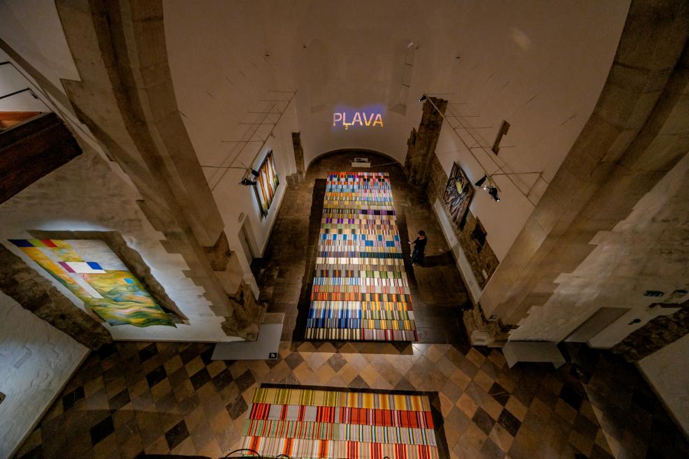 A view from above of the 'Meadow' exhibition hall with colorful fabrics on the floor and tapestries on the walls.