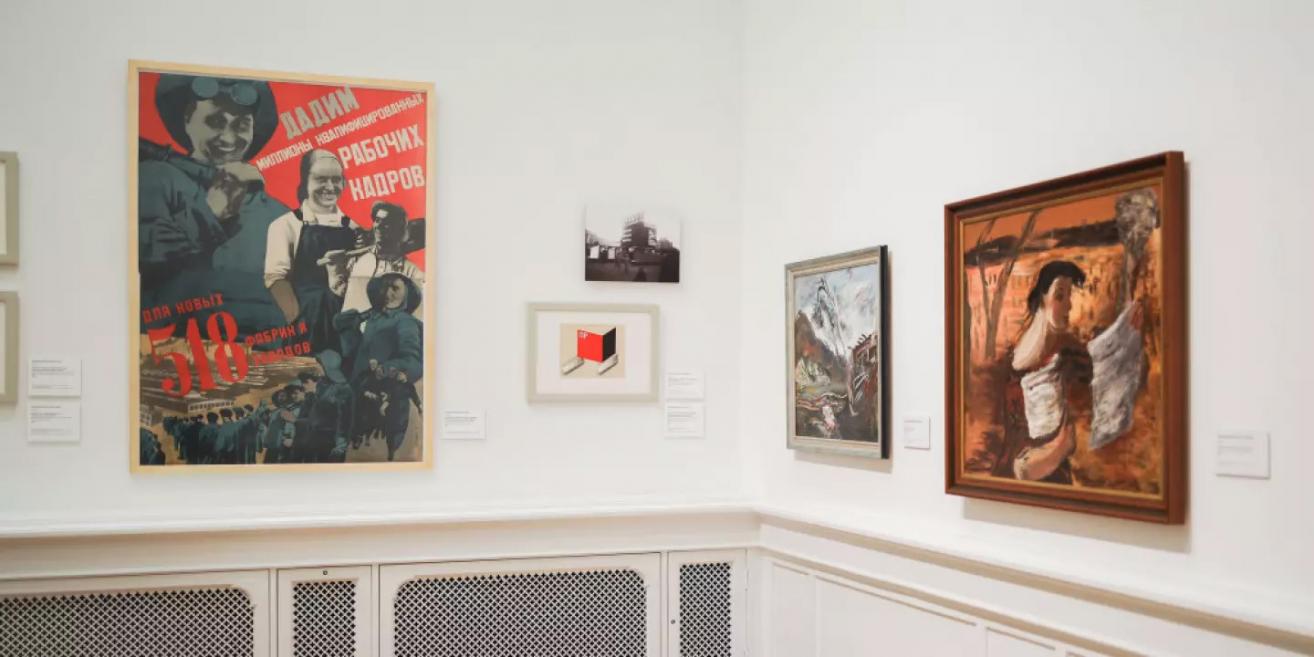 Izstādes sienas fragments ar padomju laika plakātiem un gleznojumiem, kas ataino darba tēmu un industriālo vidi.