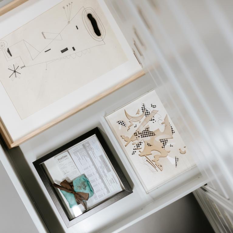 A display section with several framed abstract graphic works and a document in a display case.