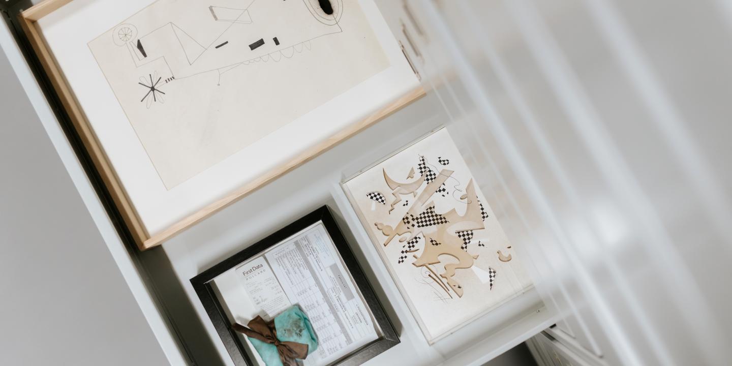 A display section with several framed abstract graphic works and a document in a display case.