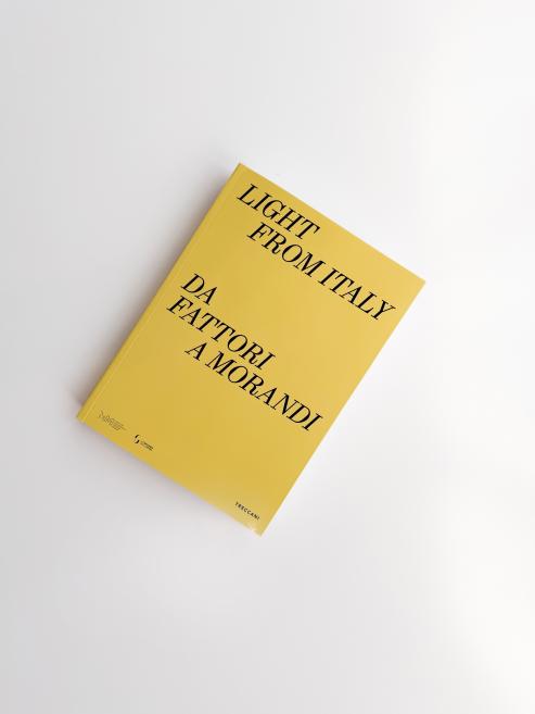 Dzeltenas krāsas grāmata ar melnu uzrakstu “Light from Italy. Da Fattori a Morandi”, fotografēta no augšas uz balta fona, grāmata novietota nedaudz slīpi.