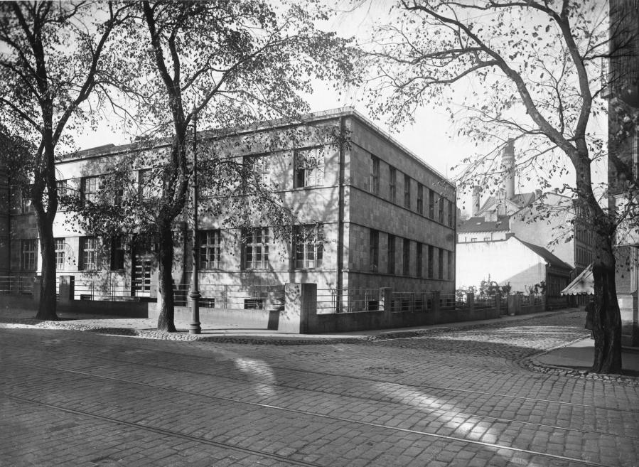 Melnbalta fotogrāfija ar Roche administratīvo ēku Rīgā, skatīta no ielas ar kokiem un bruģētu ceļu.